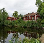 En blank damm vid Järle med röda äldre hus intill. 