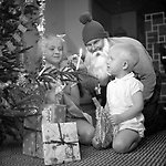 Svartvit bild. Två barn och en jultomte sitter vid en julgran